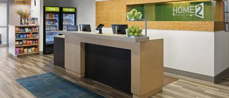A hotel reception area with a counter, a refrigerator, and a shelf with snacks.