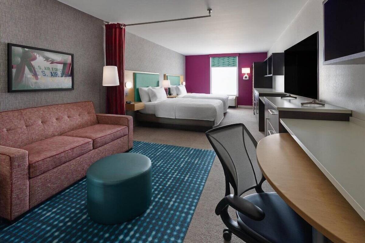 A hotel room with a sofa, two beds, a desk, a TV, and a picture of the U.S. Air Force on the wall.