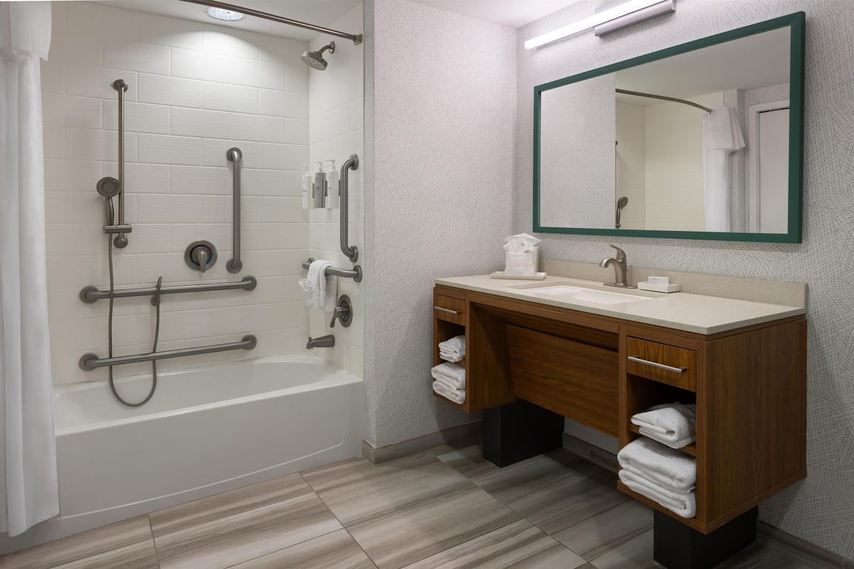 A modern bathroom with a bathtub, shower, and vanity with a mirror.