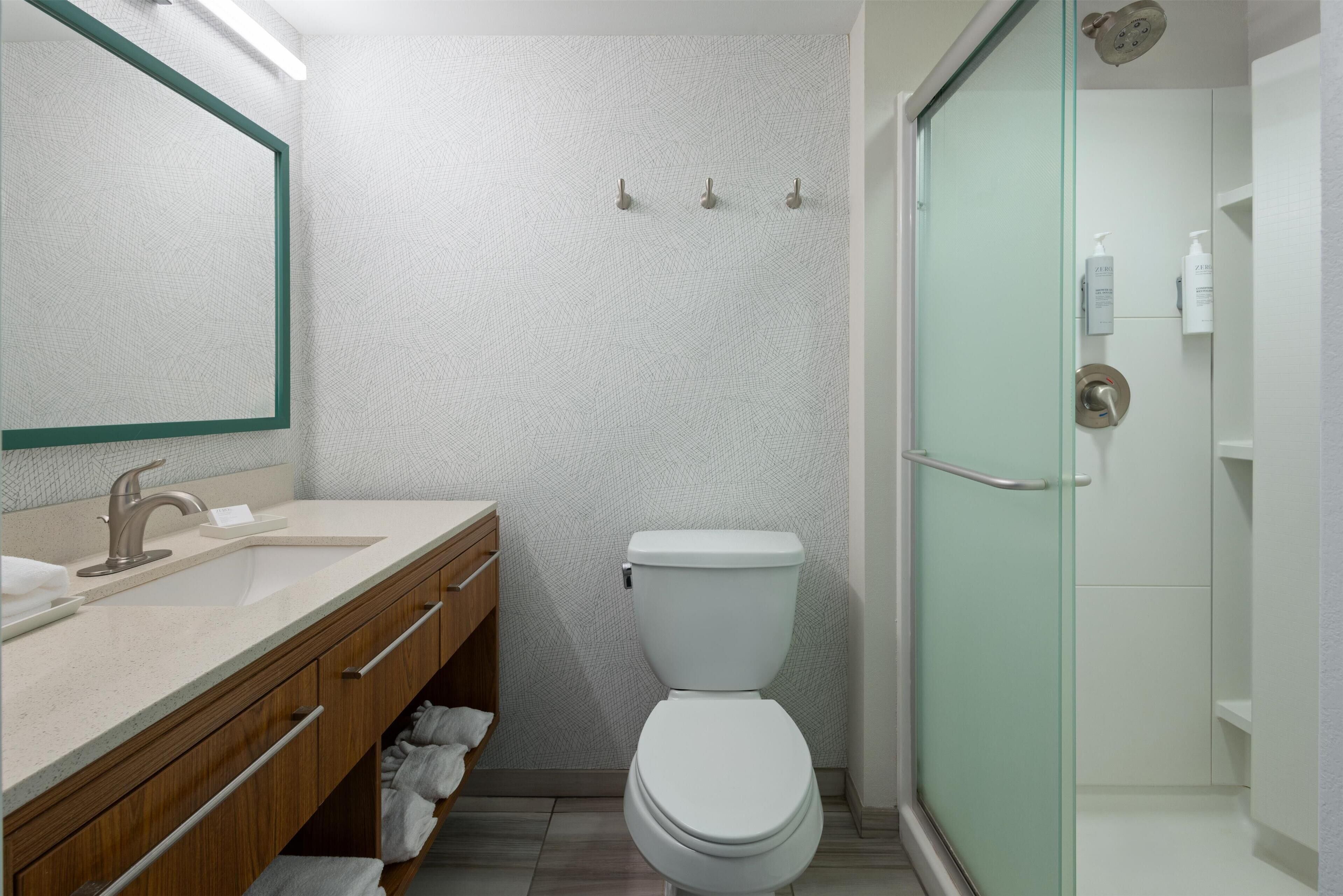 A bathroom with a white sink, wooden vanity, and a glass shower enclosure.