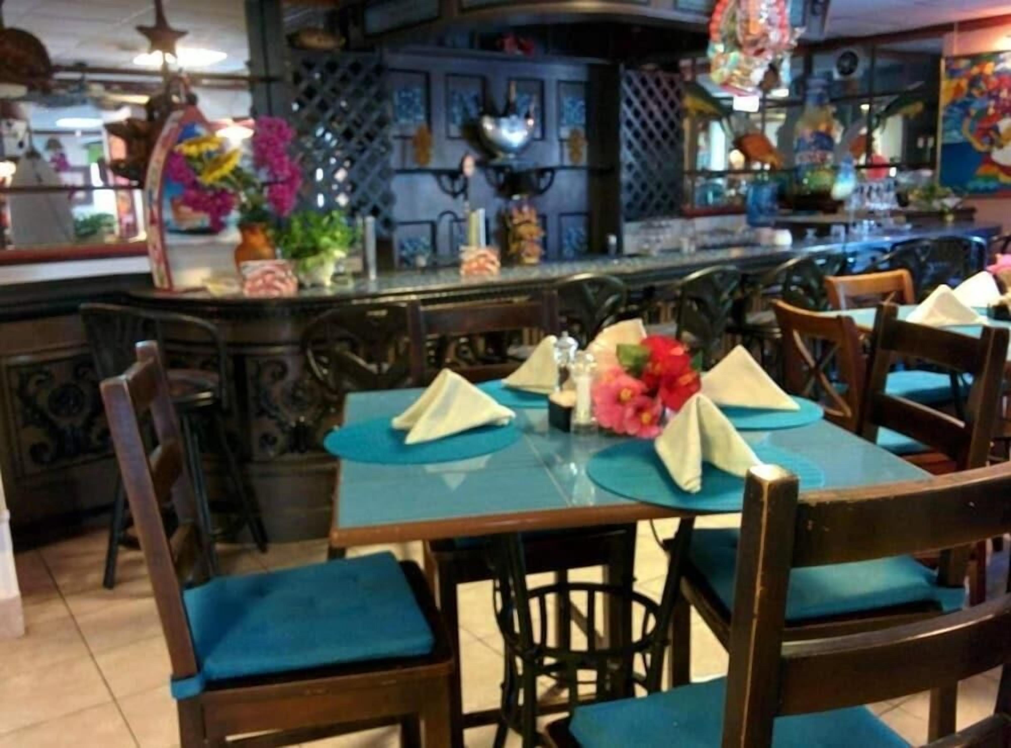 A restaurant with wooden tables and chairs, blue tablecloths, and decorative flowers.