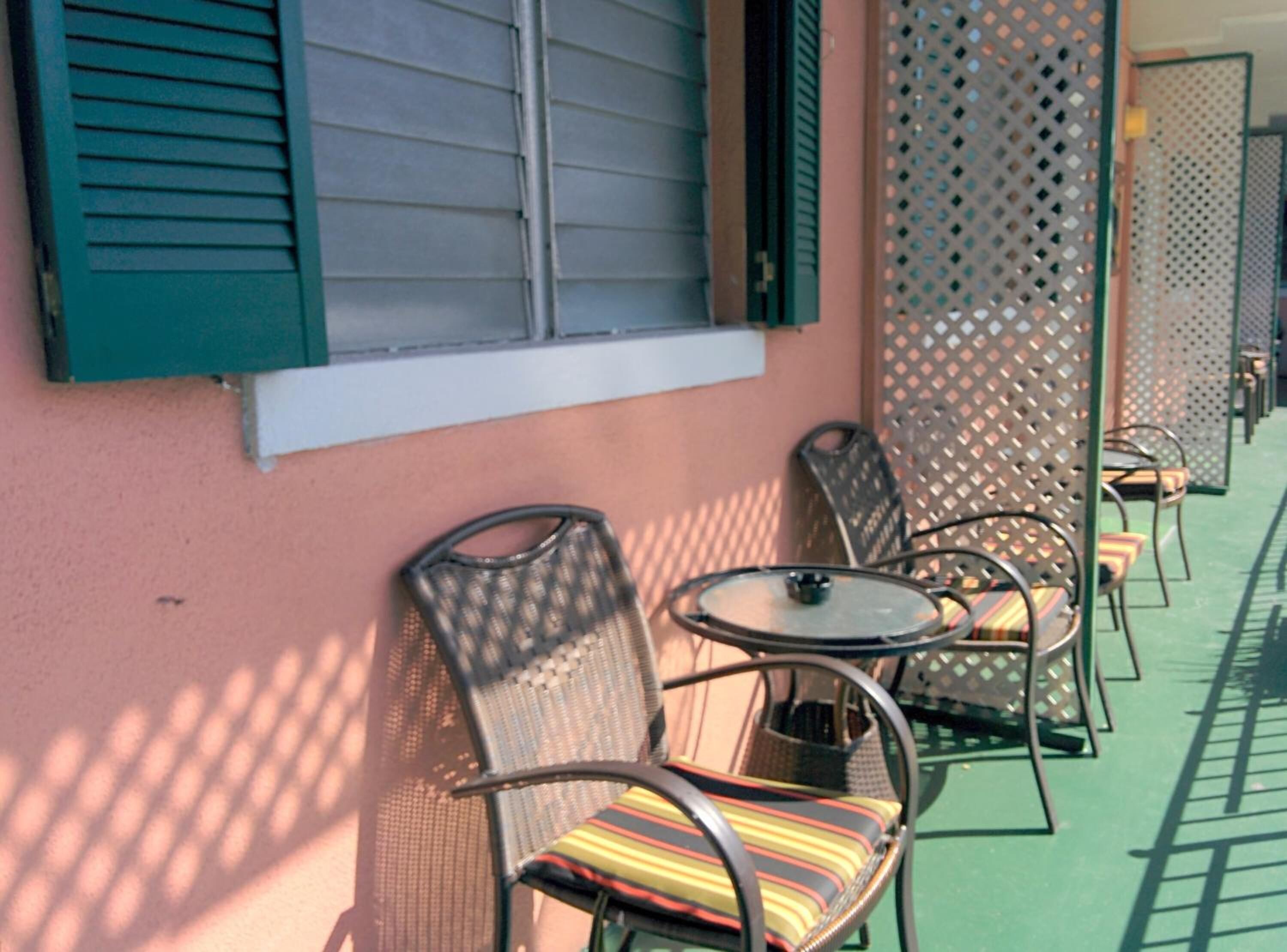 A row of outdoor seating with chairs and tables, a wall with shutters, and a patterned fence.