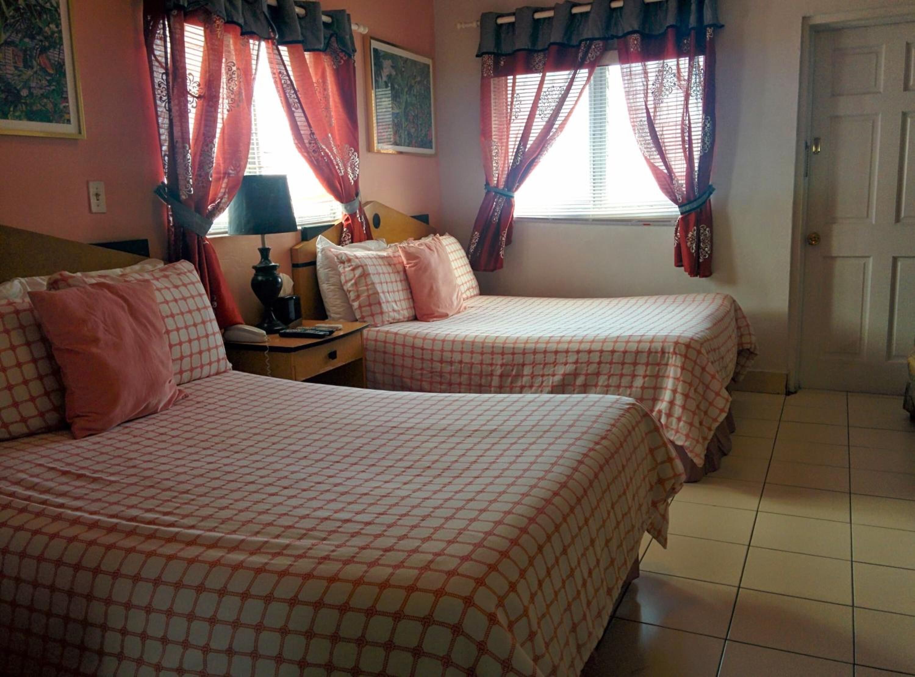 A hotel room with two beds, a nightstand, a lamp, and a door.