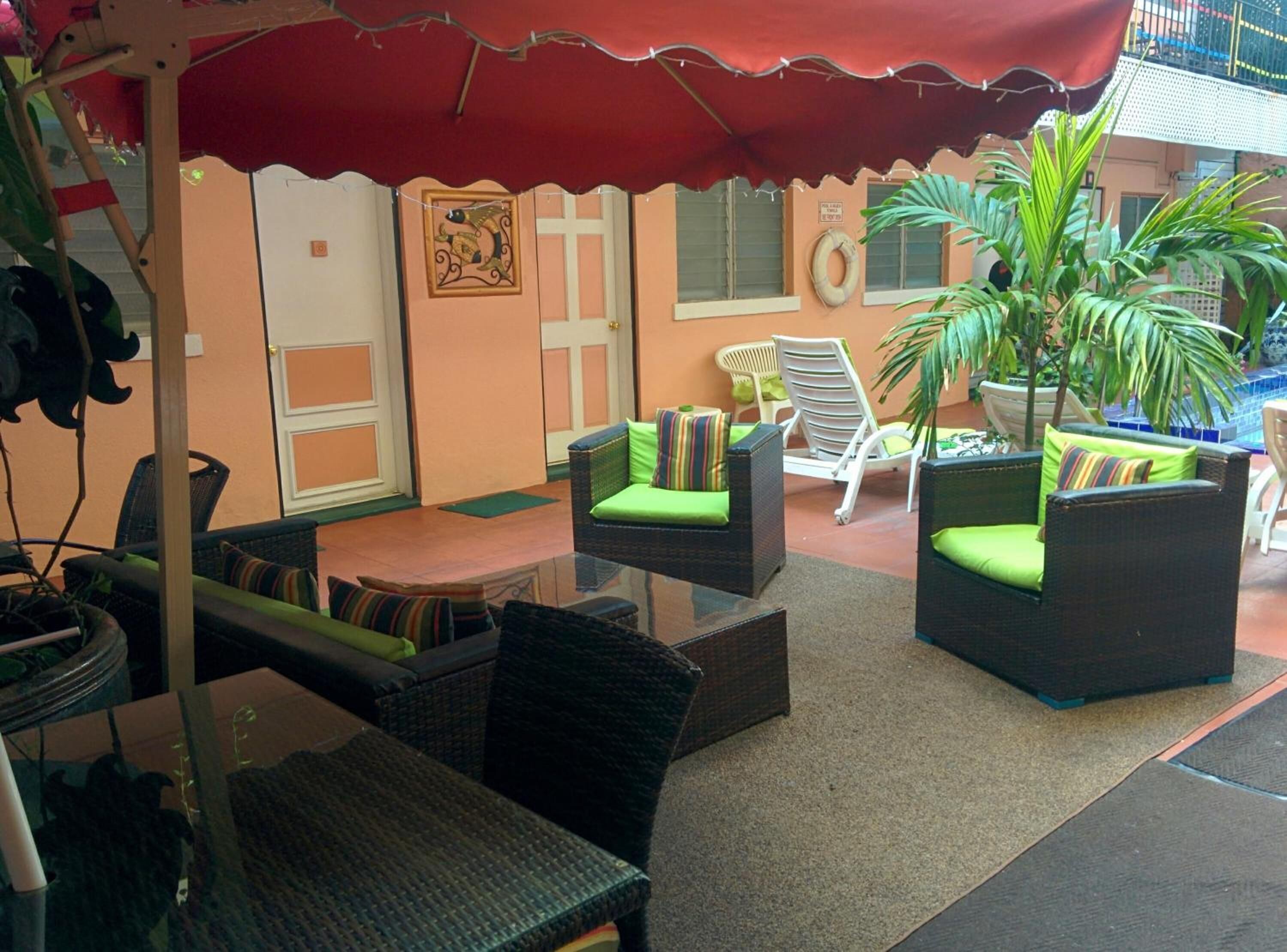 An outdoor seating area with wicker furniture and green cushions, a red umbrella, and a potted plant.