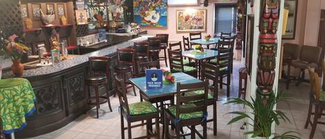 Interior de un restaurante con varias mesas y sillas, una zona de bar y diversas decoraciones, incluyendo máscaras y totems.