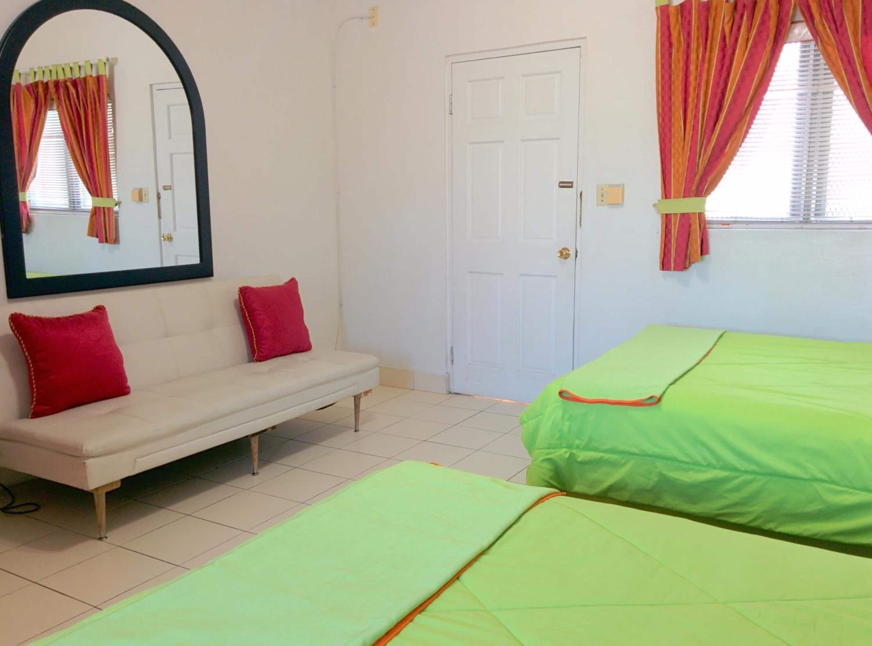Un dormitorio con un sofá blanco, dos camas verdes, una puerta blanca y un espejo con cortinas.