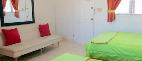 Une chambre avec un canapé blanc, deux lits verts, une porte blanche et un miroir agrémenté de rideaux.