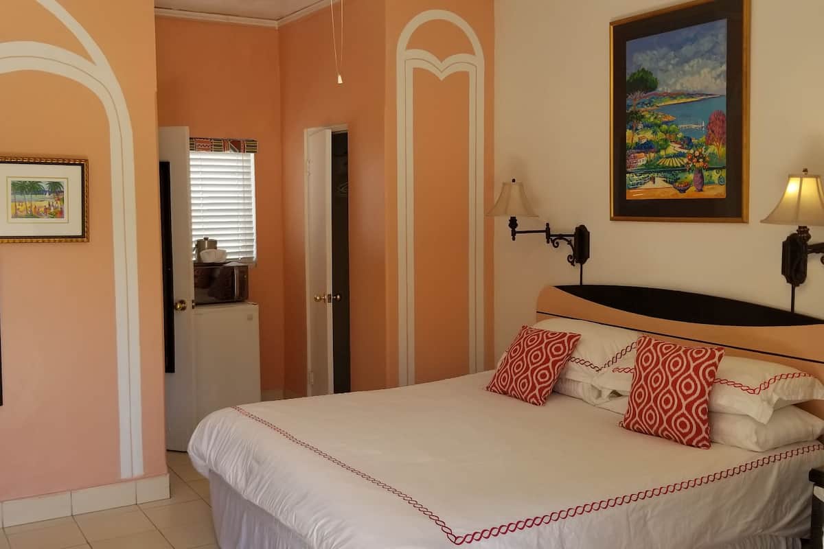 A hotel room with a bed, a television, a painting, and a door leading to a bathroom.