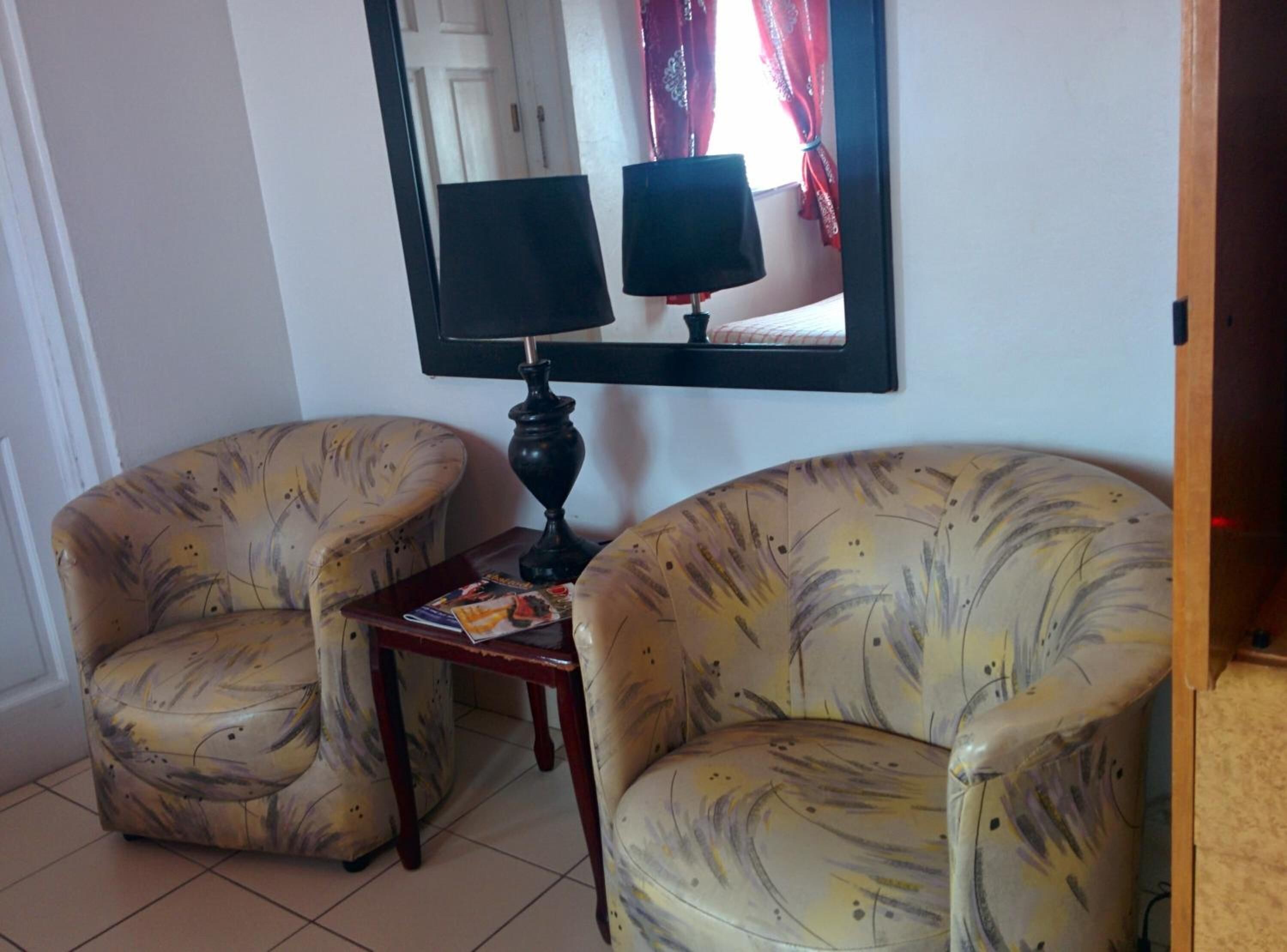 A room with two armchairs and a small table, a mirror with a lamp, and a door in the background.