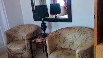 A room with two armchairs and a small table, a mirror with a lamp, and a door in the background.