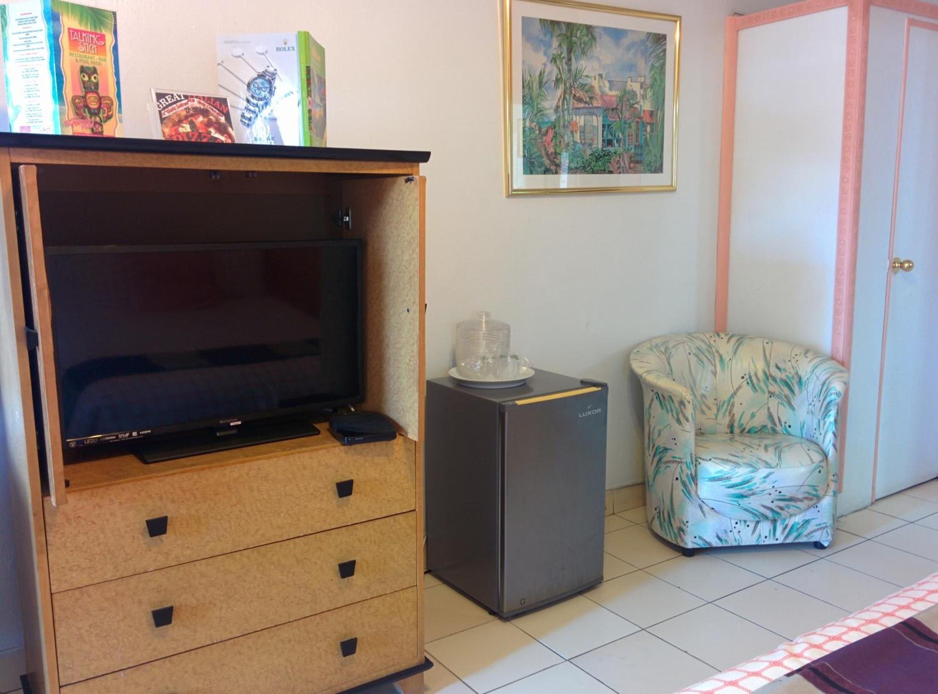 A room with a TV, a small fridge, a chair, and a painting on the wall.
