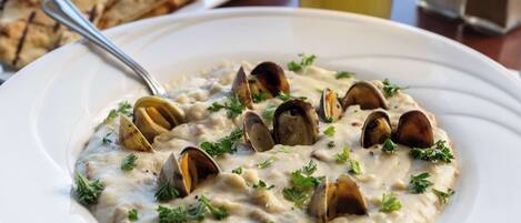 A white plate with a creamy seafood dish garnished with parsley, accompanied by grilled bread and a glass of beverage.