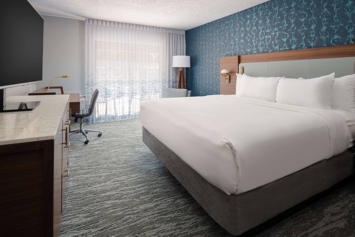 A hotel room with a large bed, a desk with a computer, a chair, and a television.