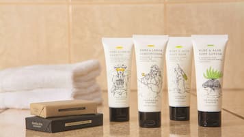 Fyra tuber med produkter från Cascadia Soapery och två tvålbitar på en hylla i badrummet.
