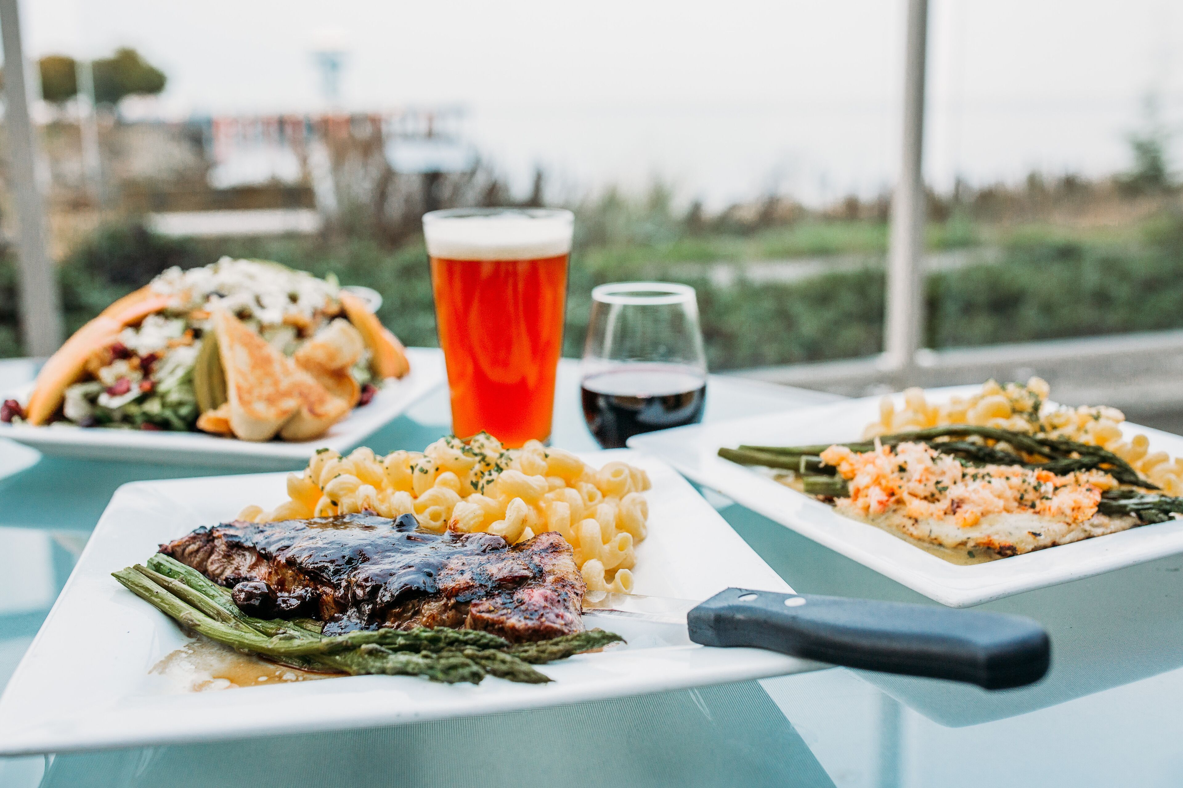 A table with three plates of food, a knife, and two glasses of beverages.