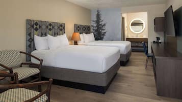 A hotel room with two beds, a desk, a chair, a TV, and a bathroom visible through an open door.