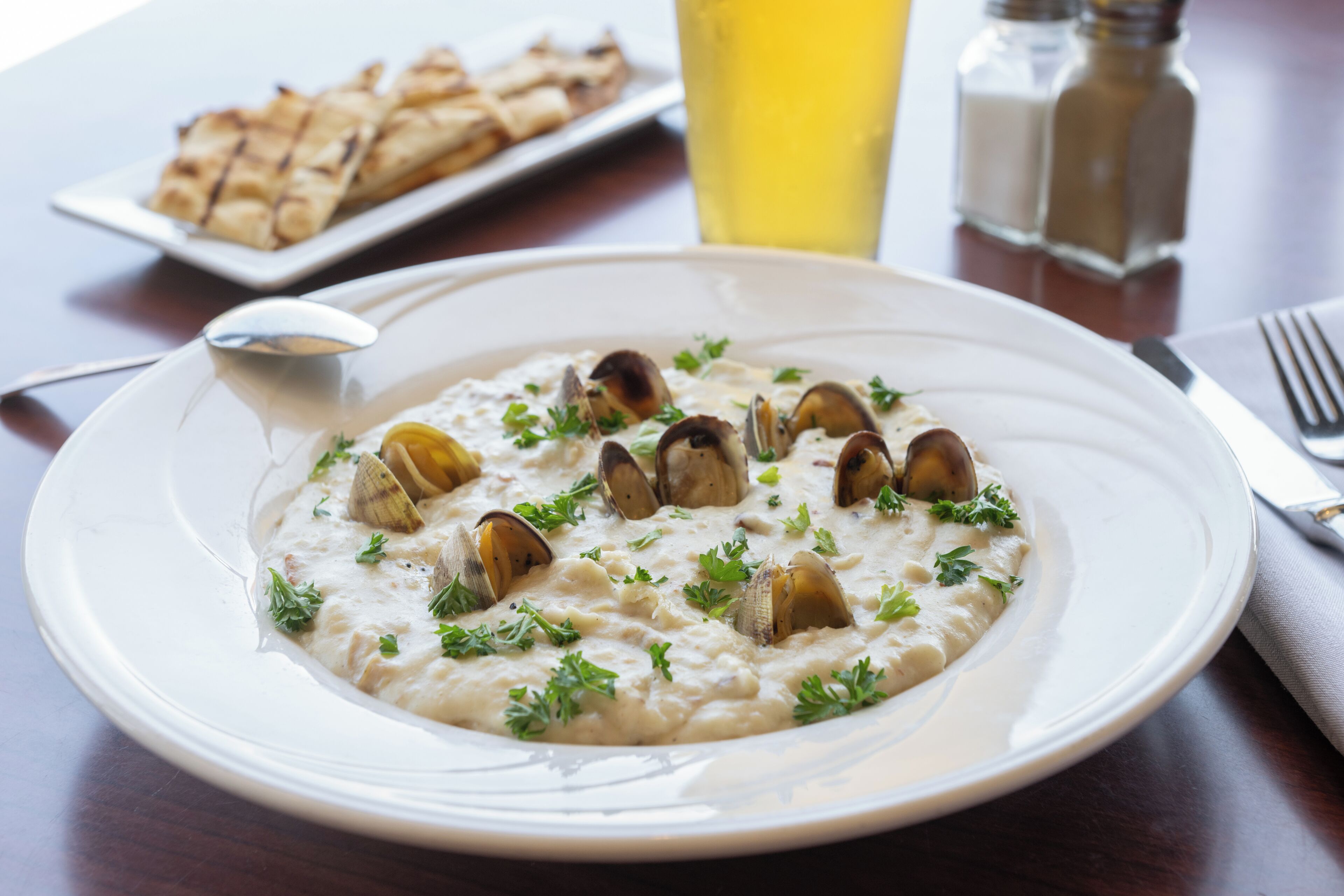 Un plato de risotto de mariscos adornado con perejil, un vaso de bebida amarilla y un plato de pan sobre una mesa de madera.