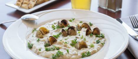 Un plato de risotto de mariscos adornado con perejil, un vaso de bebida amarilla y un plato de pan sobre una mesa de madera.
