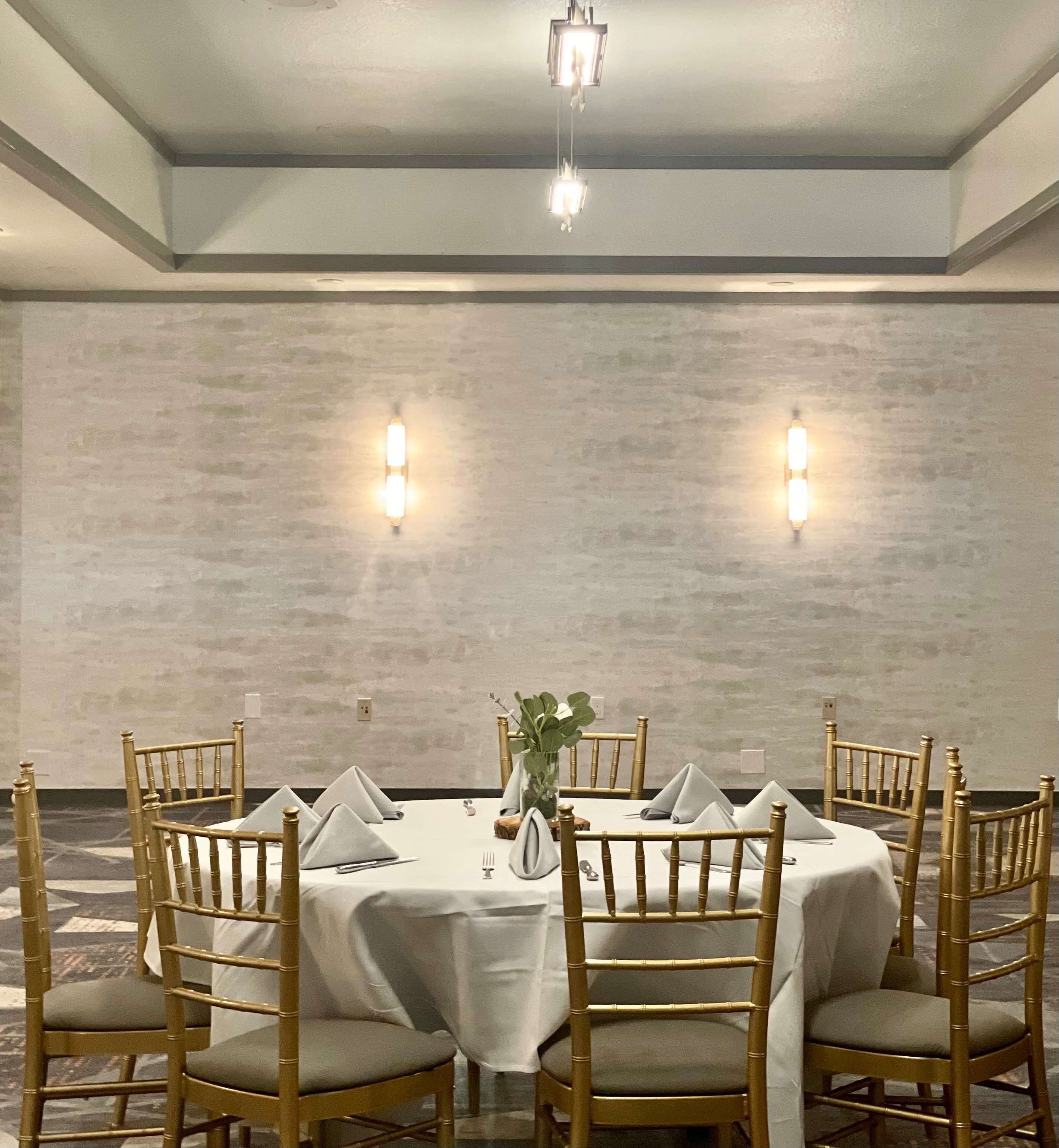 A dining area with a round table, gold chairs, and two wall-mounted lights.