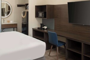Habitación de hotel con una cama grande, un escritorio con computadora, televisión y microondas.