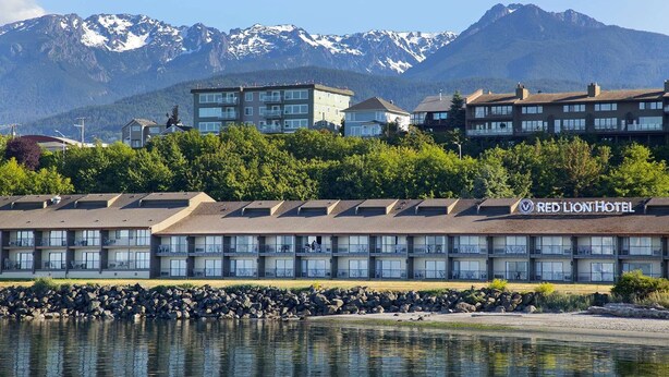 A hotel with multiple floors, a rocky shoreline, and a mountain backdrop.