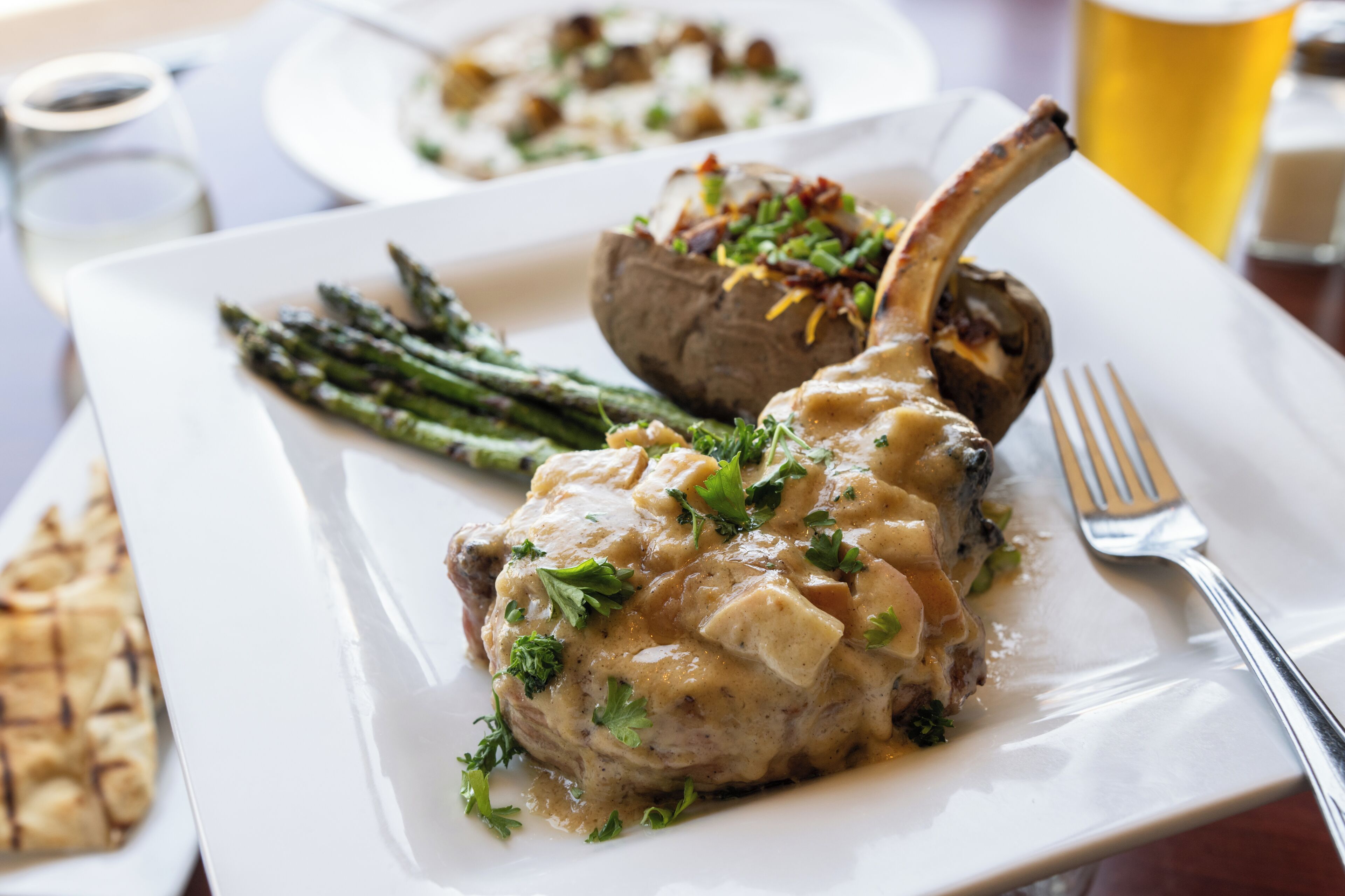 A plate with a lamb chop, asparagus, and a baked potato topped with cheese and herbs.