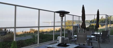Une terrasse extérieure avec des tables et des chaises, un foyer et une vue sur l’eau et les bâtiments éloignés.