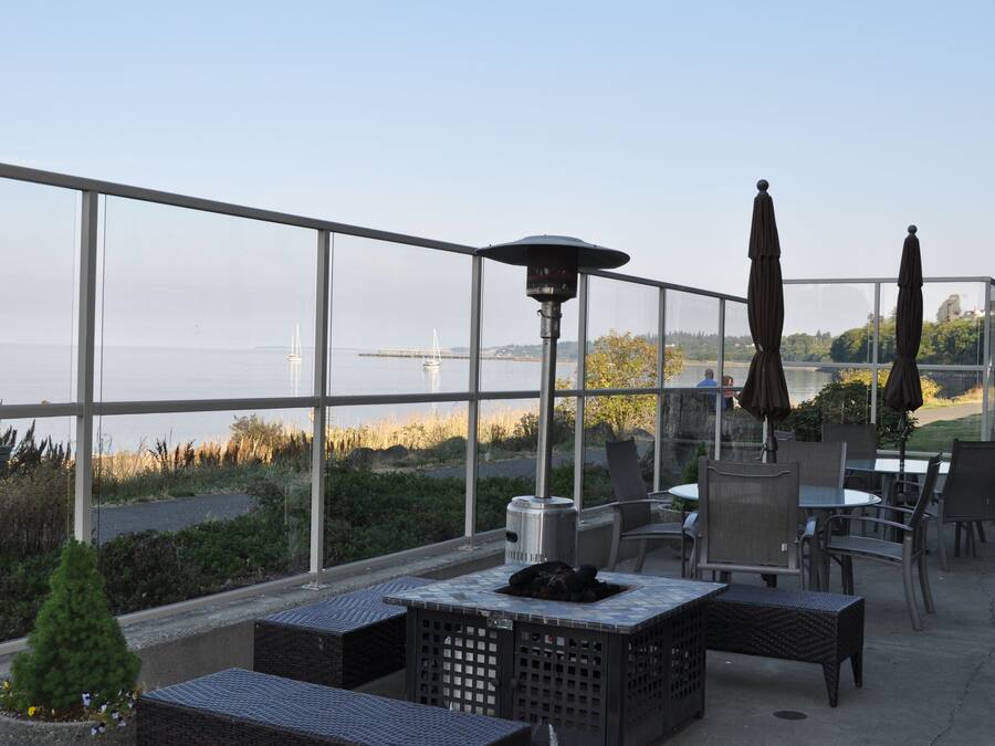 An outdoor patio with tables and chairs, a fire pit, and a view of the water and distant buildings.