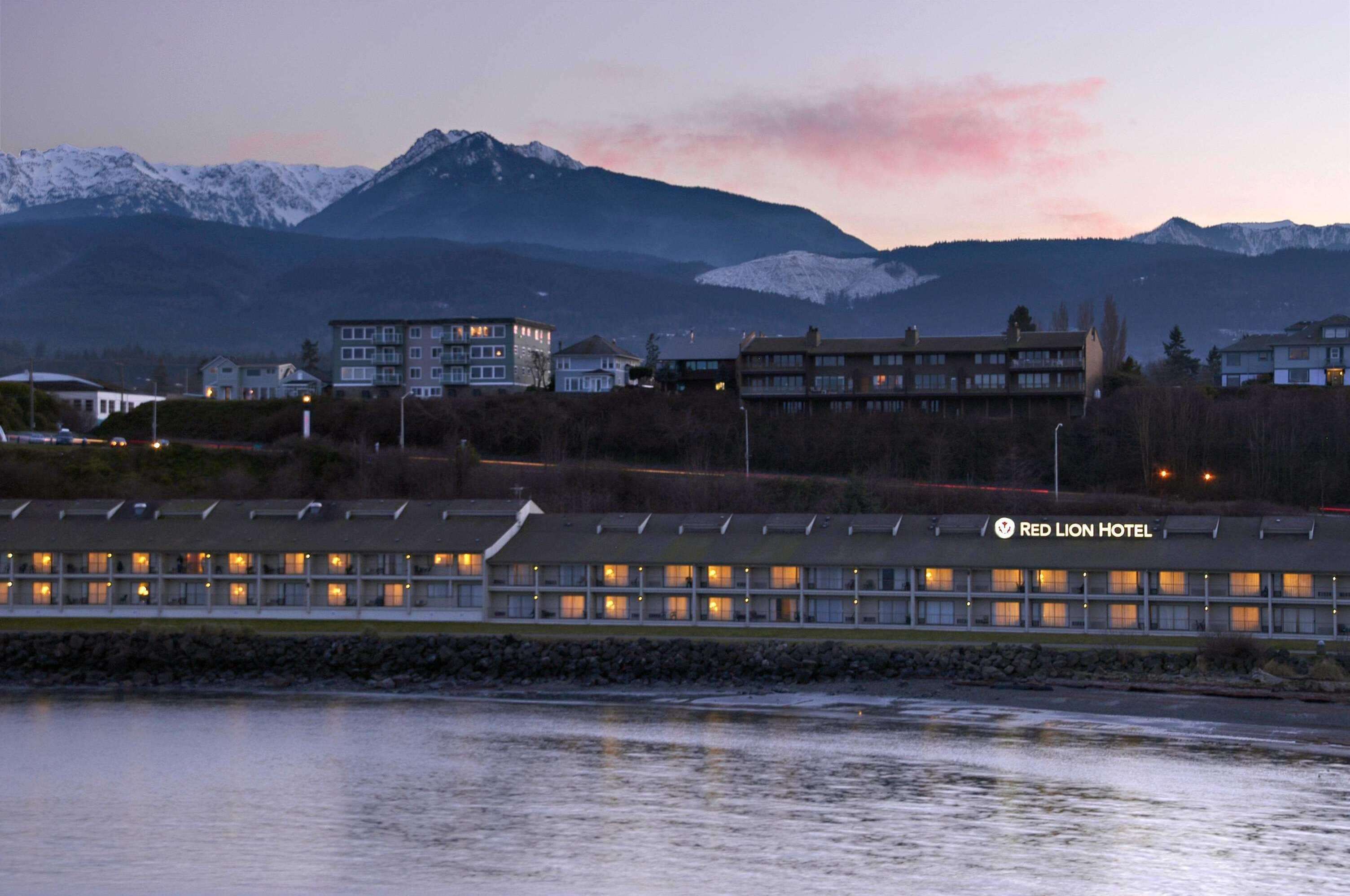 Un hotel con varias construcciones, vistas a montañas y una masa de agua al frente.