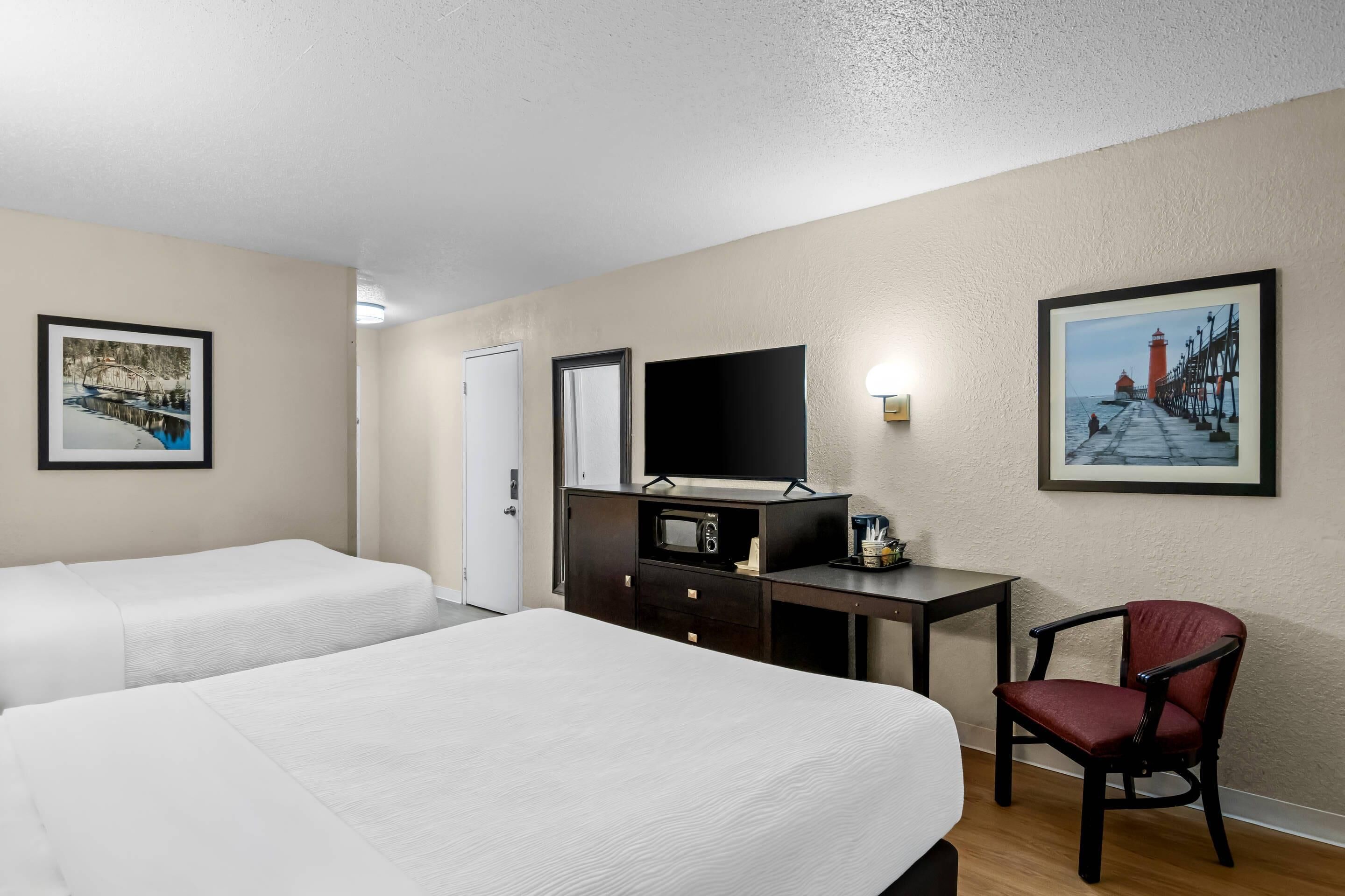 A hotel room with two beds, a desk, a TV, and a chair.