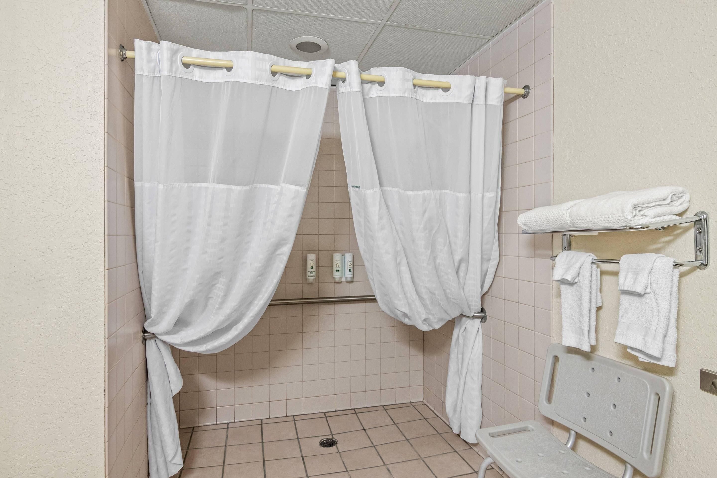 A shower with white curtains, a white towel rack, and a white bench.