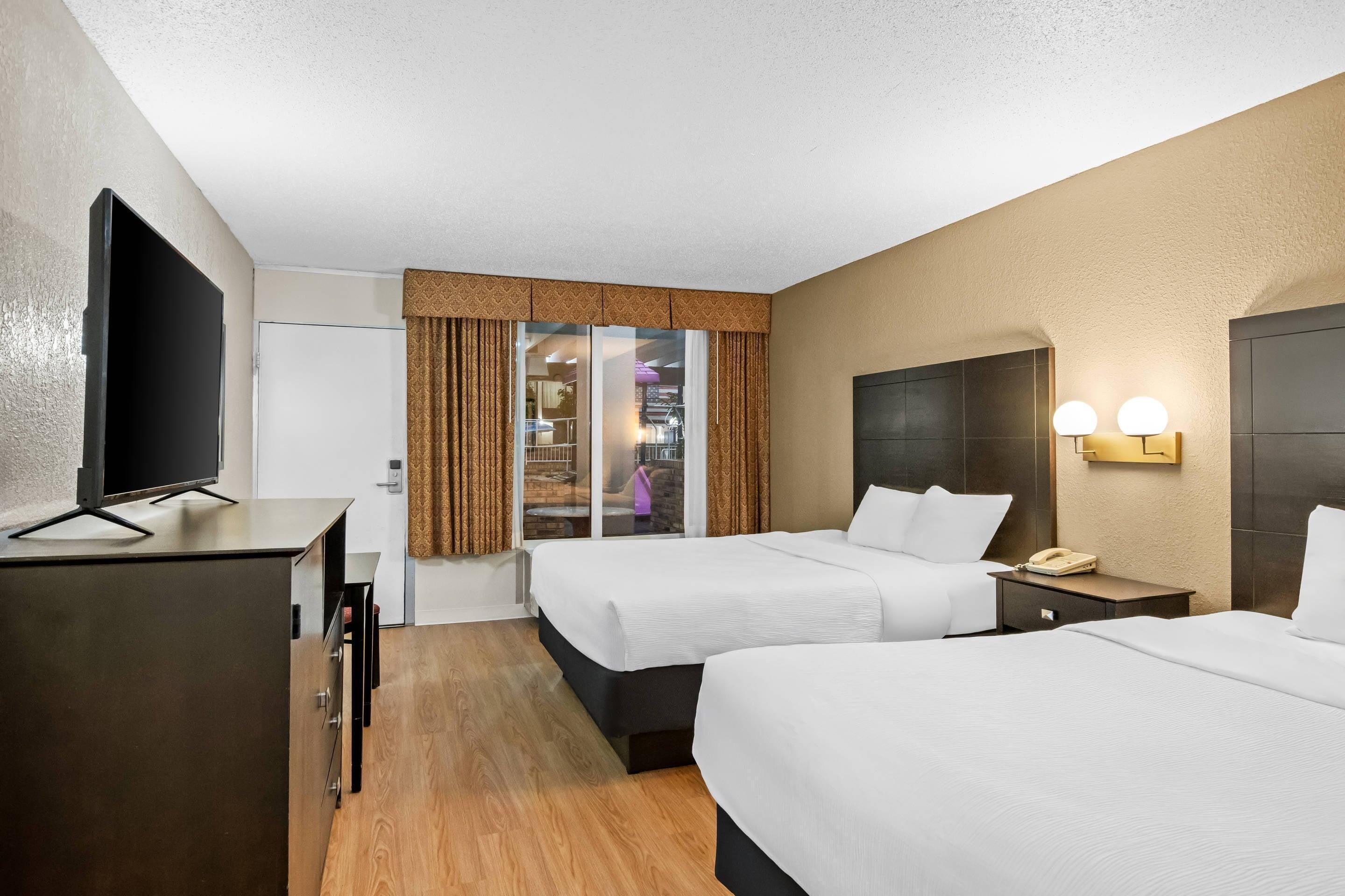A hotel room with two beds, a desk, a TV, and a sliding door to a balcony.