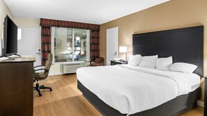A hotel room with a bed, desk, chair, TV, and a window with curtains. - Quality Inn & Suites (Grayling)