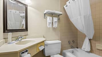 Baño con lavamanos, inodoro y bañera. Se ve un perchero con toallas y una cortina de ducha.