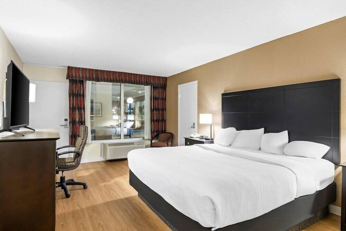 A hotel room with a bed, a desk, a chair, a TV, and a window with curtains.