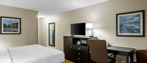 Une chambre d’hôtel avec un lit, un bureau et une chaise, une télévision et des tableaux encadrés aux murs.