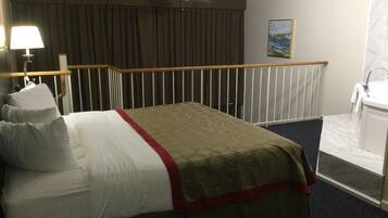 Una habitación de hotel con cama, ventilador de techo, baño con lavamanos y un cuadro en la pared.