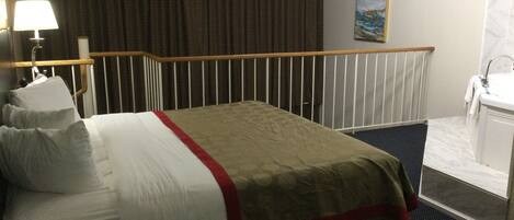 A hotel room with a bed, a ceiling fan, a bathroom with a sink, and a painting on the wall.