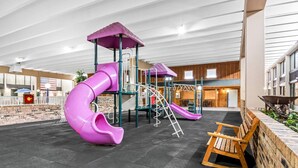An indoor playground with a purple slide, a wooden bench, and a brick wall. - Quality Inn & Suites (Grayling)