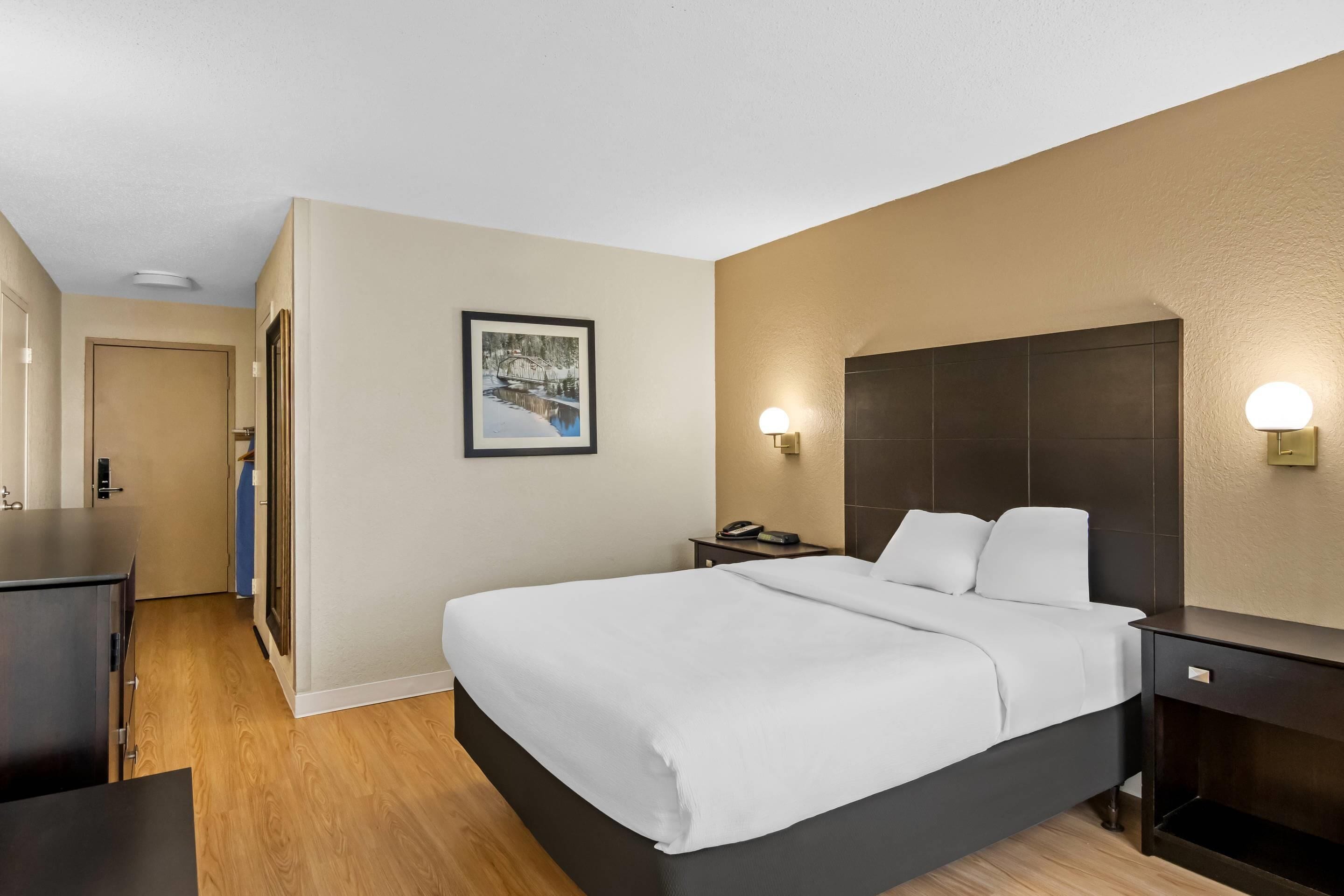 A hotel room with a bed, bedside tables, a desk, and a framed picture on the wall.