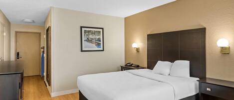 A hotel room with a bed, bedside tables, a desk, and a framed picture on the wall.