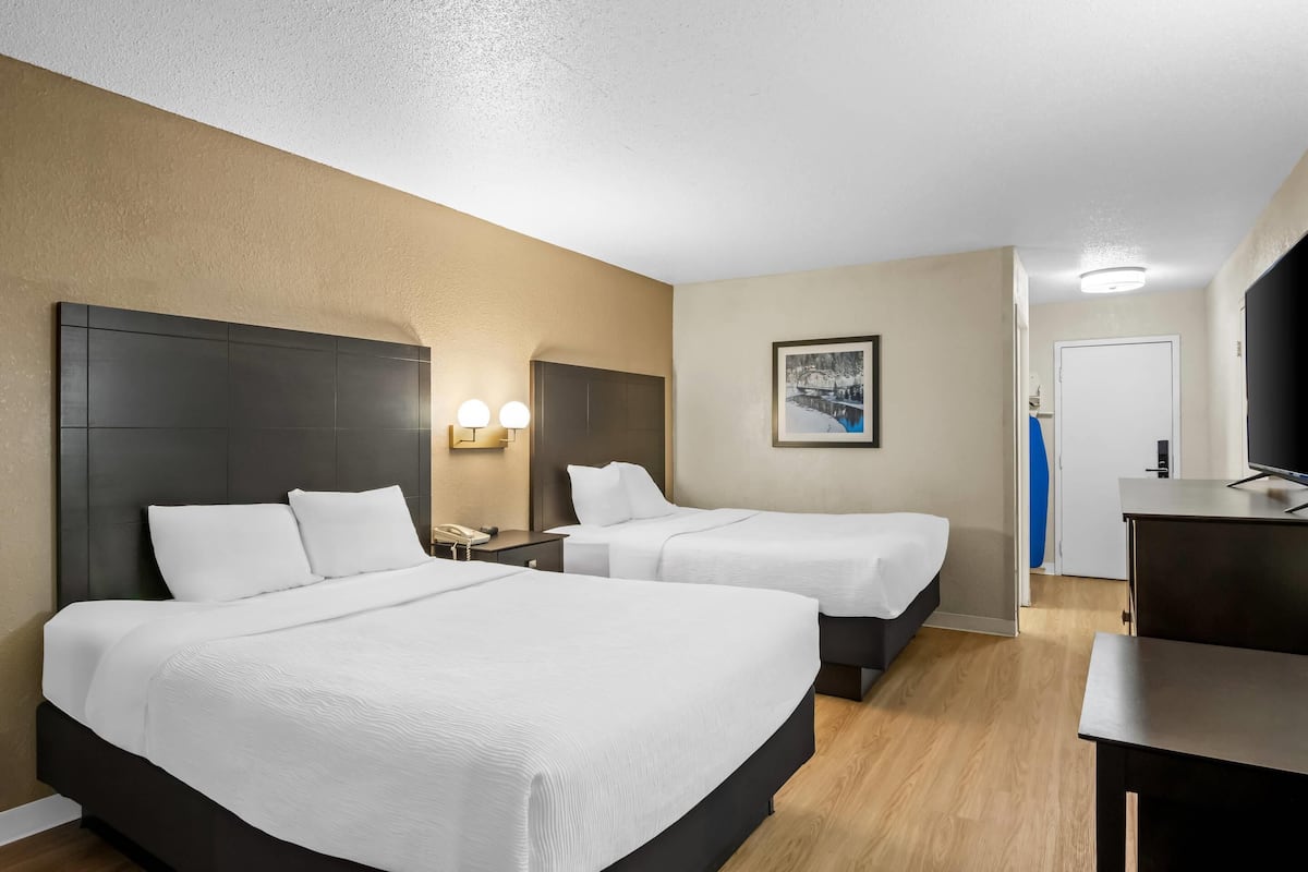 A hotel room with two beds, a desk, a mirror, and a picture on the wall.