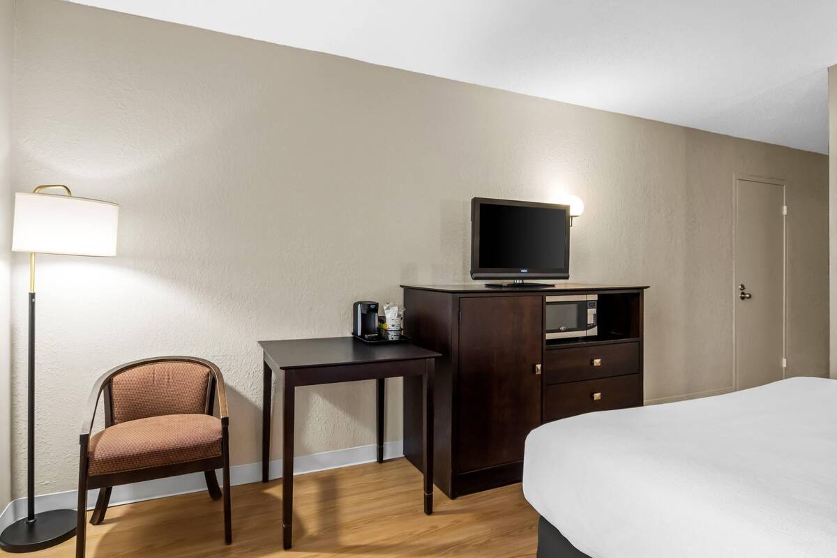 A hotel room with a bed, a desk, a chair, a television, a cabinet, and a floor lamp.