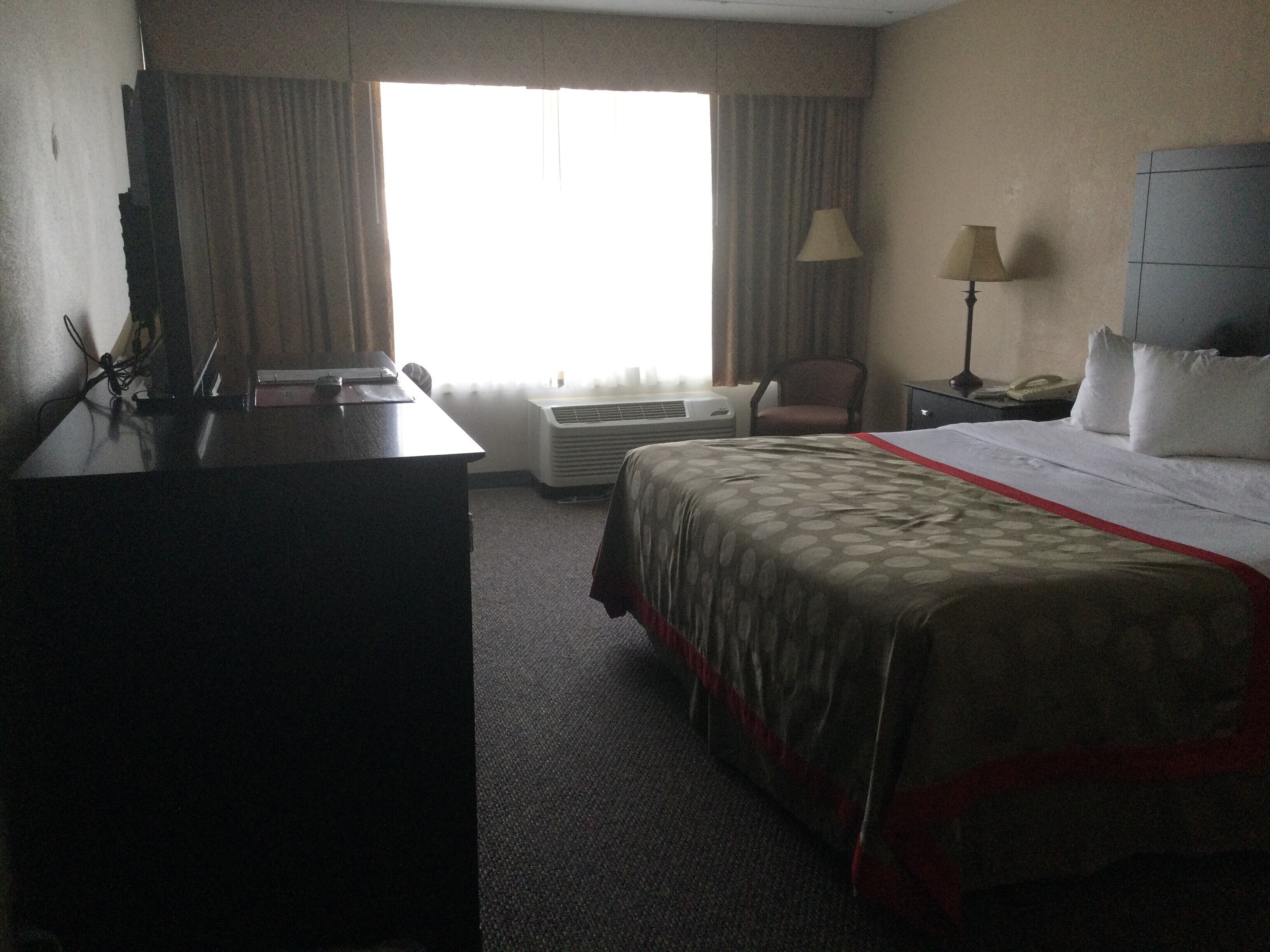 Habitación de hotel con cama, escritorio, aire acondicionado, silla y lámpara.