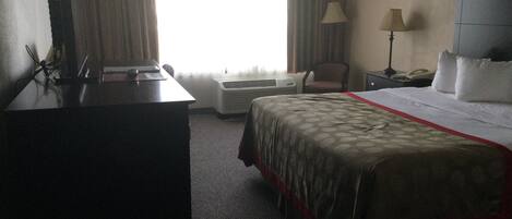 Ein Hotelzimmer mit Bett, Schreibtisch, Klimaanlage, Stuhl und Lampe.