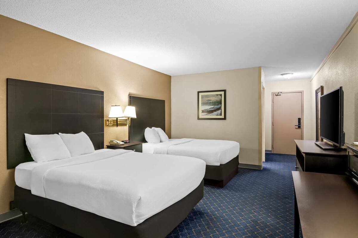 A hotel room with two beds, a TV, a desk, and a painting on the wall.