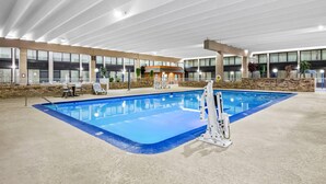 An indoor swimming pool with a clear view of the pool area, a lifeguard stand, and a seating area with chairs. - Quality Inn & Suites (Grayling)