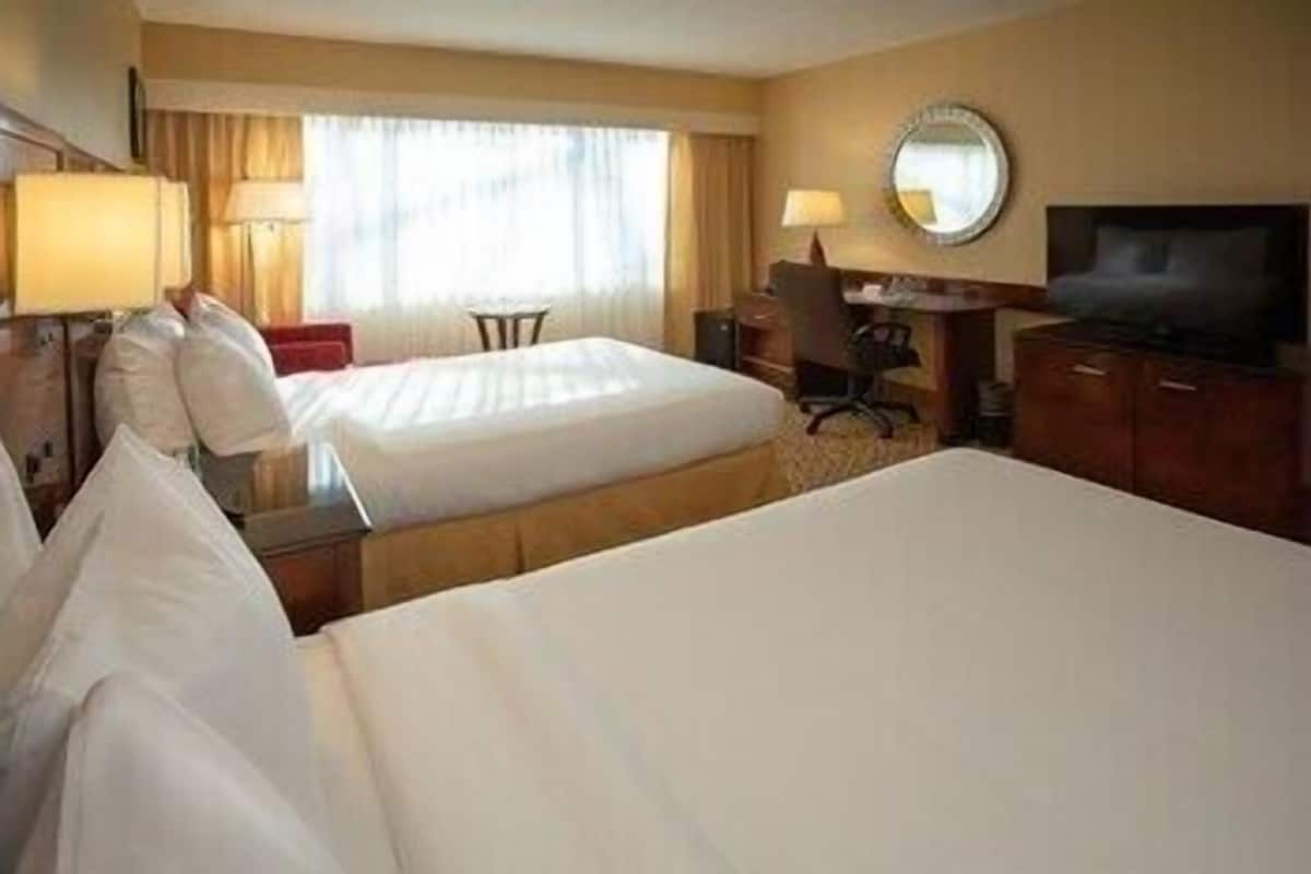 Habitación de hotel con dos camas, un escritorio, una silla, un televisor y un ventanal con cortinas.