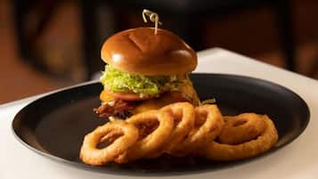A burger with a bun, lettuce, tomato, and a piece of bacon, accompanied by onion rings on a plate.