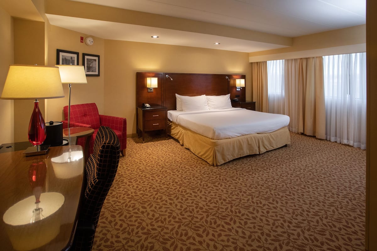 Habitación de hotel con una cama grande, un escritorio con lámpara, una silla y una ventana con cortinas.